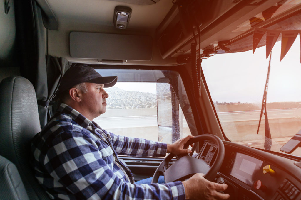 Driver in cabin of big modern truck vehicle on highway